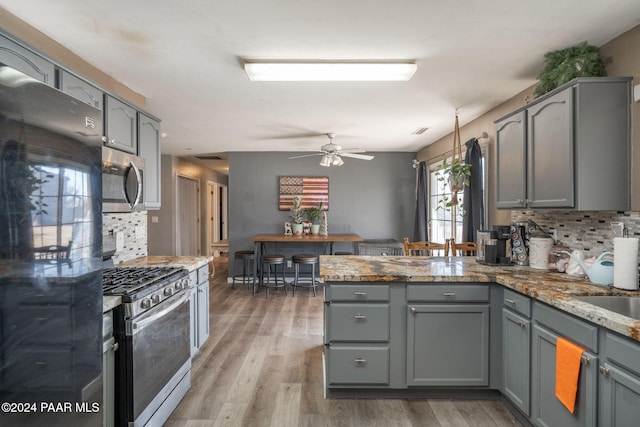 kitchen featuring appliances with stainless steel finishes, backsplash, light hardwood / wood-style floors, and gray cabinets