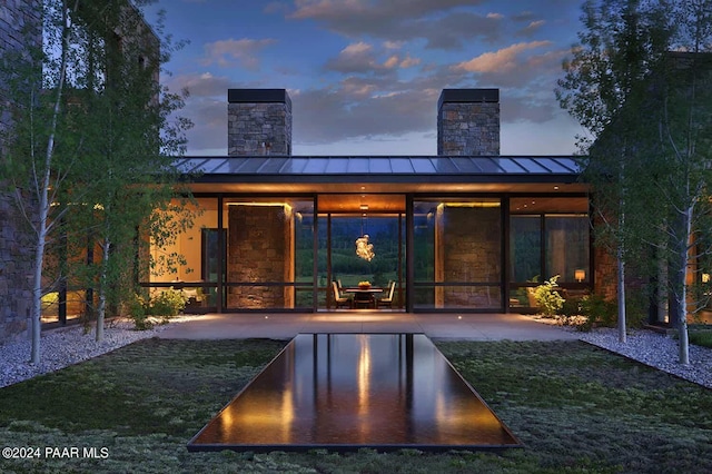 back house at dusk featuring a patio and a lawn