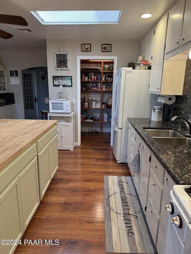 kitchen featuring a skylight, white appliances, dark wood-type flooring, sink, and dark stone countertops