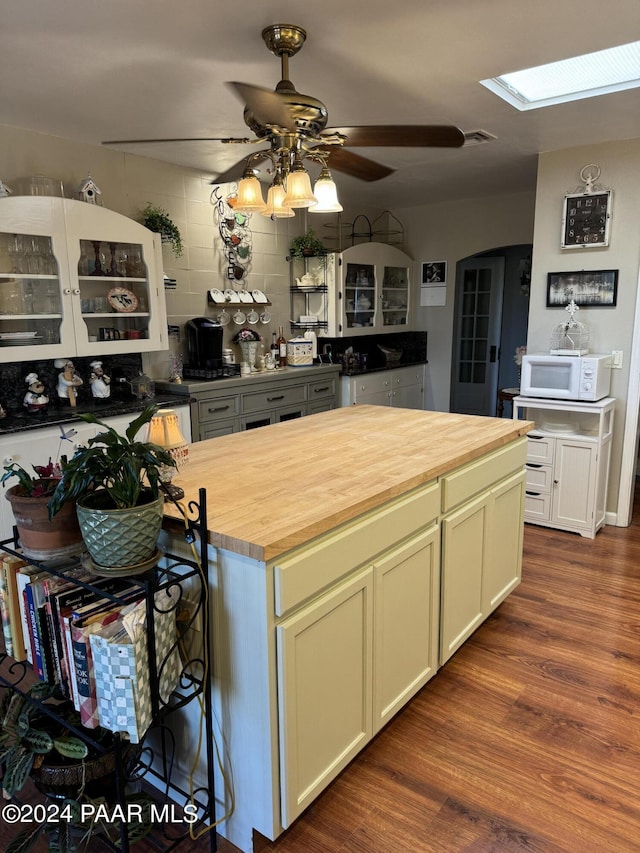 kitchen featuring a skylight, ceiling fan, dark wood-type flooring, wood counters, and backsplash