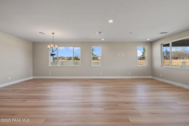 empty room with a notable chandelier, a healthy amount of sunlight, and light hardwood / wood-style flooring