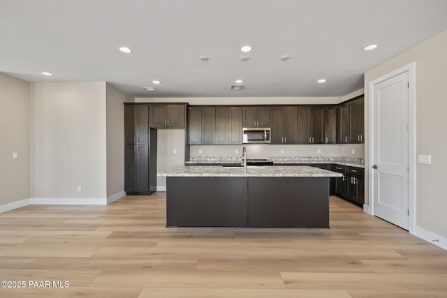 kitchen featuring sink, light stone counters, light hardwood / wood-style floors, a kitchen island with sink, and dark brown cabinets