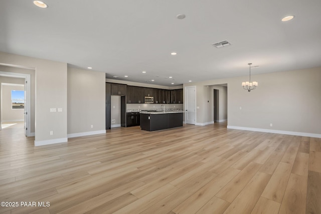 unfurnished living room with sink, a chandelier, and light wood-type flooring