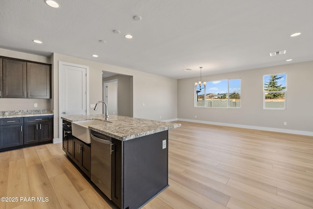 kitchen with sink, an inviting chandelier, light stone counters, decorative light fixtures, and a center island with sink