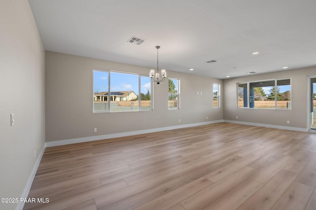 spare room featuring plenty of natural light, an inviting chandelier, and light wood-type flooring