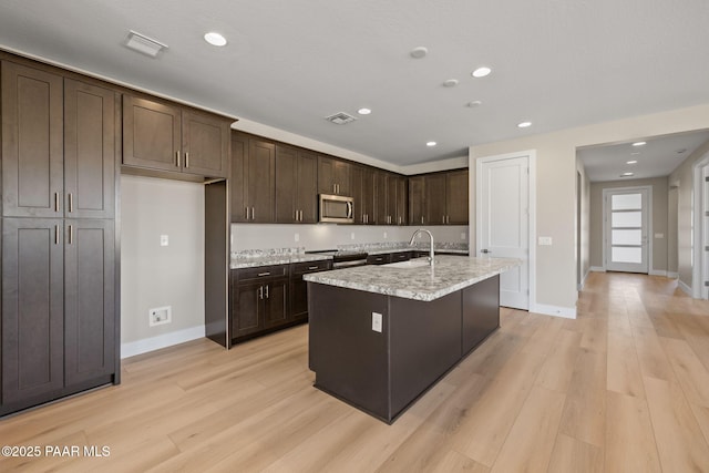 kitchen featuring dark brown cabinets, light hardwood / wood-style floors, sink, and an island with sink