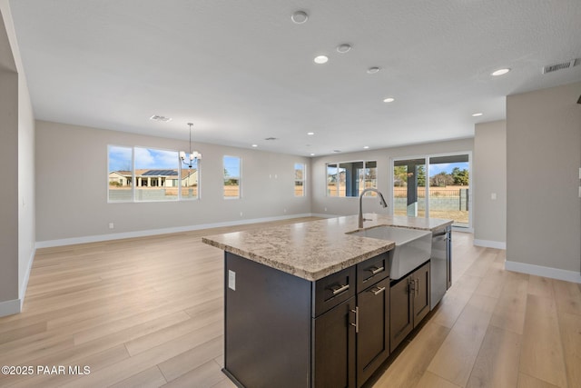 kitchen with dishwasher, an inviting chandelier, sink, light wood-type flooring, and an island with sink