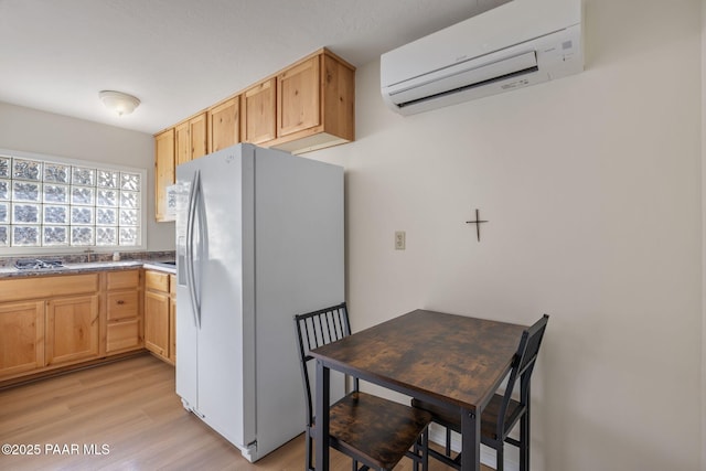 kitchen with a wall unit AC, light wood finished floors, stainless steel gas cooktop, light brown cabinetry, and white refrigerator with ice dispenser