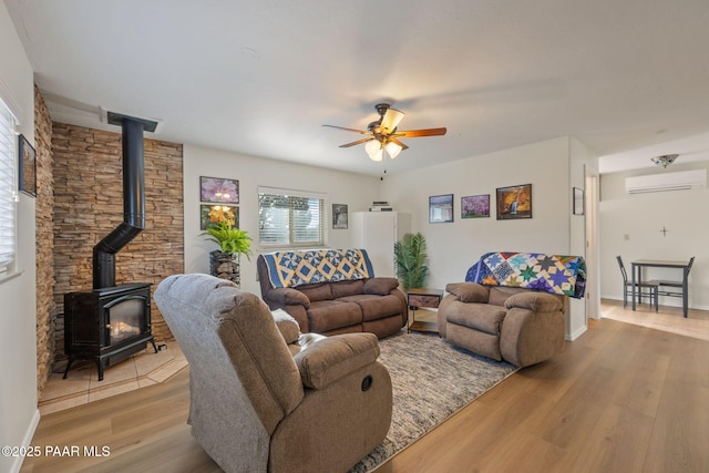 living area with wood finished floors, baseboards, a wall mounted AC, a wood stove, and ceiling fan