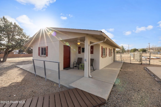 view of property exterior featuring stucco siding, a patio, a ceiling fan, and a gate