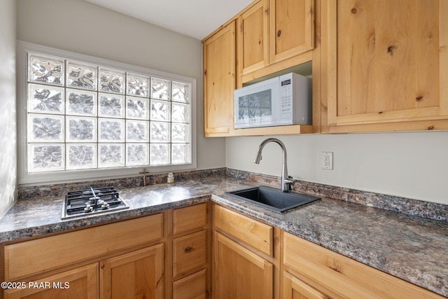 kitchen featuring white microwave, stainless steel gas cooktop, dark stone counters, and a sink