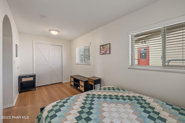 bedroom featuring wood finished floors, arched walkways, and baseboards