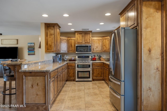 kitchen featuring a breakfast bar, light stone counters, brown cabinets, a peninsula, and stainless steel appliances