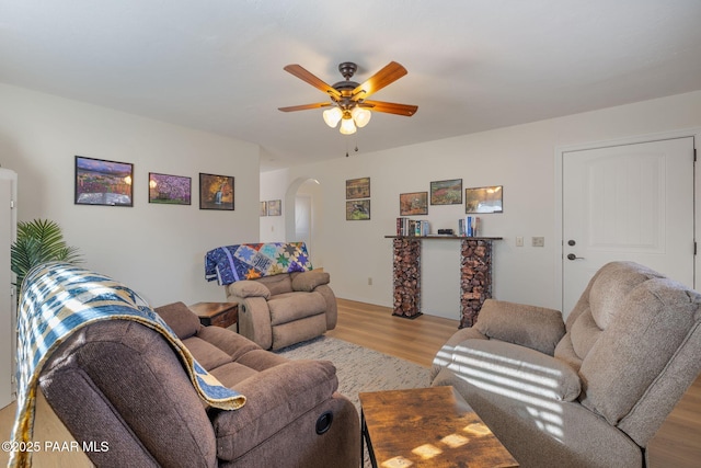 living area with a ceiling fan, arched walkways, and light wood finished floors