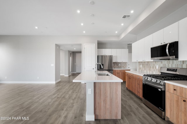 kitchen with white cabinets, stainless steel appliances, light hardwood / wood-style flooring, and a center island with sink