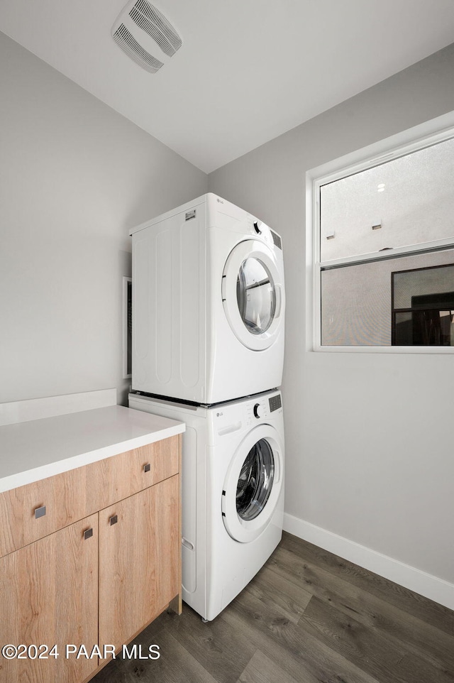 clothes washing area with cabinets, dark wood-type flooring, and stacked washer and clothes dryer