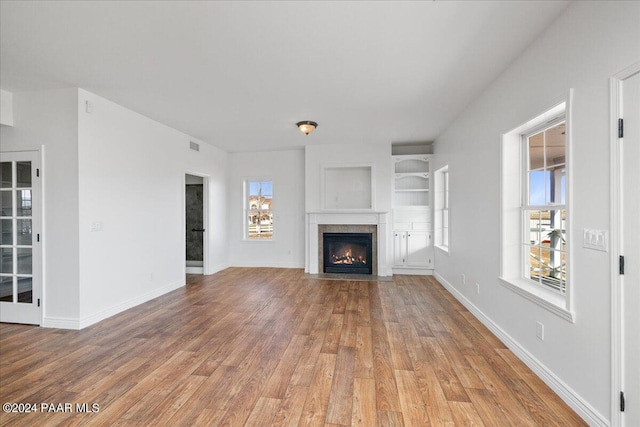 unfurnished living room with hardwood / wood-style flooring, a wealth of natural light, and built in features