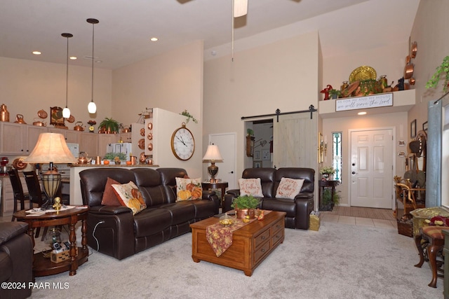 living room featuring a towering ceiling, a barn door, light colored carpet, and ceiling fan