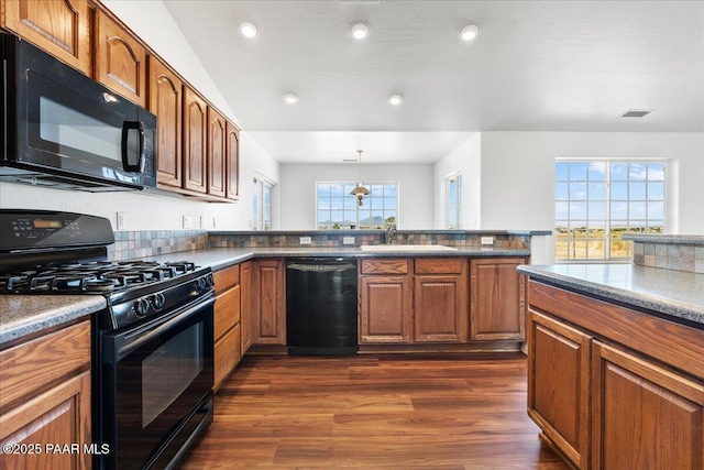 kitchen featuring a sink, brown cabinetry, black appliances, dark wood-type flooring, and visible vents
