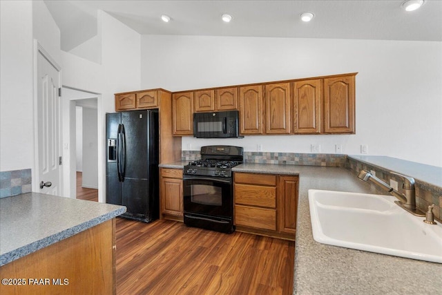 kitchen featuring dark wood-type flooring, a sink, brown cabinets, and black appliances
