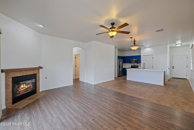1735 Oro Dr, Cottonwood, AZ 86326 - unfurnished living room with arched walkways, a ceiling fan, a tiled fireplace, baseboards, and a sink