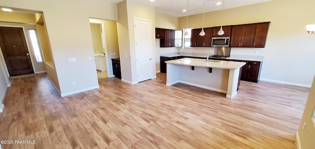 kitchen with pendant lighting, sink, dark brown cabinets, light hardwood / wood-style floors, and a kitchen bar