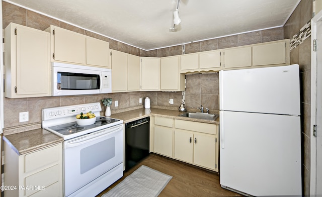 kitchen with sink, dark hardwood / wood-style flooring, cream cabinetry, track lighting, and white appliances