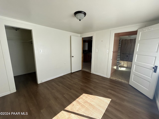 unfurnished bedroom with a walk in closet, a closet, and dark hardwood / wood-style floors