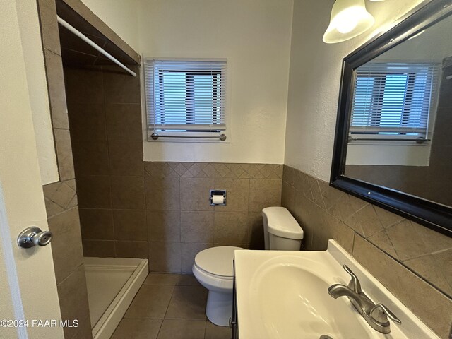 bathroom with sink, tiled shower, tile walls, tile patterned flooring, and toilet