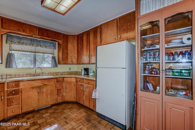 kitchen with brown cabinetry, a sink, light countertops, and freestanding refrigerator