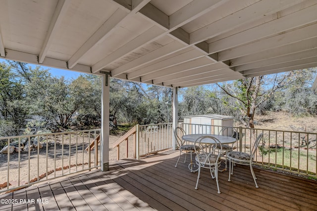 wooden deck with an outbuilding, a shed, and outdoor dining space