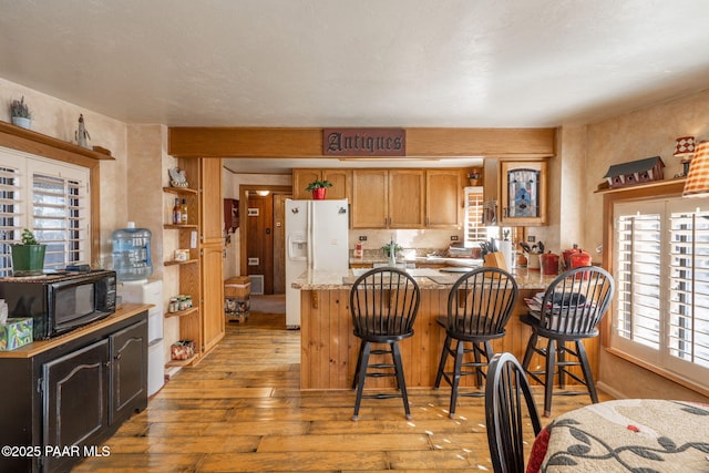 kitchen with a breakfast bar, a wealth of natural light, white refrigerator with ice dispenser, and kitchen peninsula