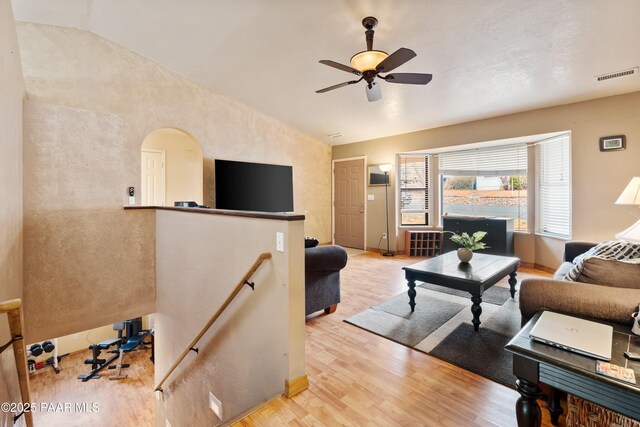 living room featuring arched walkways, visible vents, vaulted ceiling, wood finished floors, and baseboards