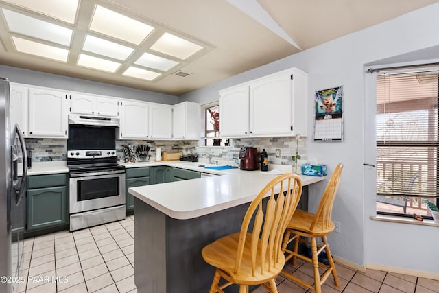 kitchen featuring a peninsula, under cabinet range hood, light tile patterned floors, and appliances with stainless steel finishes