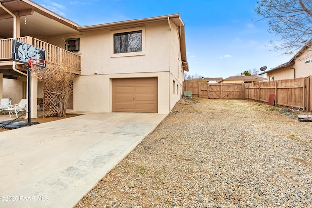 exterior space featuring stucco siding, fence, a balcony, a garage, and driveway