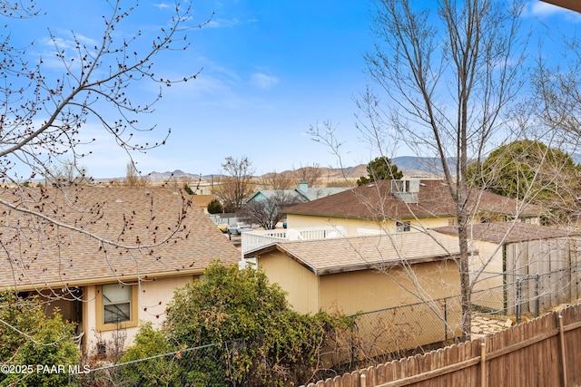 exterior space featuring a shingled roof, stucco siding, a mountain view, and fence