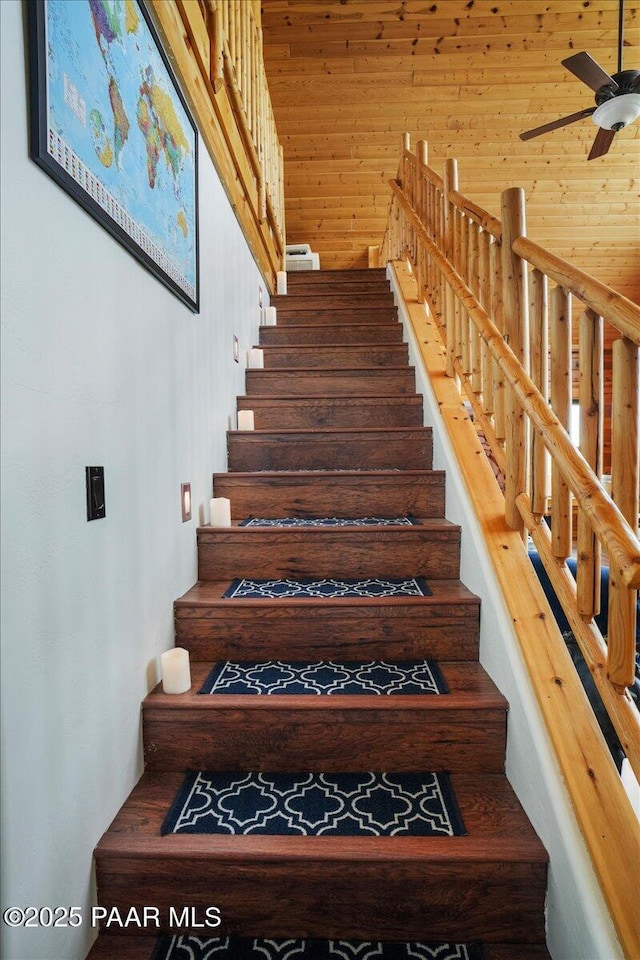 stairs with ceiling fan and wood walls