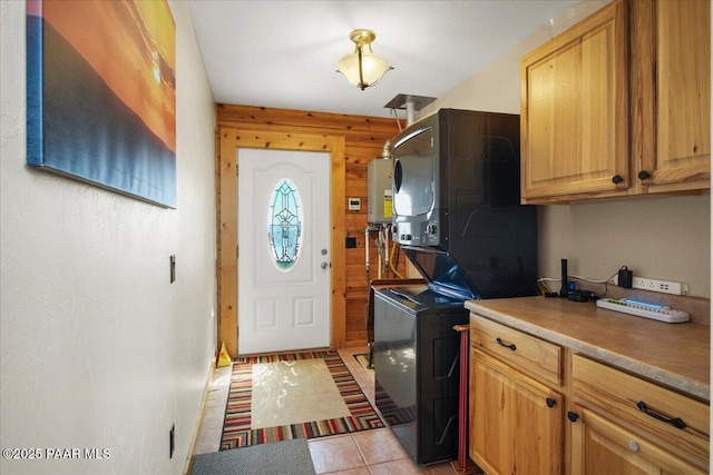 laundry room with wood walls, light tile patterned floors, cabinets, water heater, and stacked washer and clothes dryer