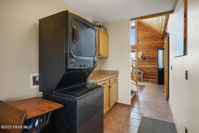 washroom featuring stacked washing maching and dryer, cabinets, light tile patterned flooring, wood walls, and plenty of natural light