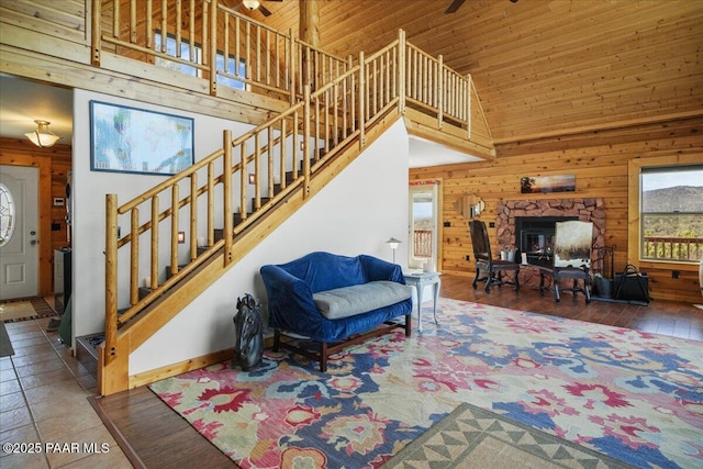 living room featuring wooden walls, high vaulted ceiling, ceiling fan, wooden ceiling, and a stone fireplace