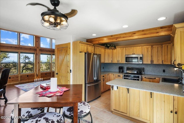 kitchen with appliances with stainless steel finishes, kitchen peninsula, light tile patterned floors, decorative backsplash, and sink