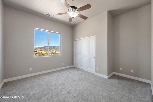 unfurnished bedroom with light carpet, a mountain view, a closet, and ceiling fan