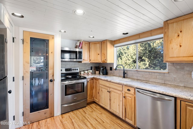 kitchen with appliances with stainless steel finishes, sink, light stone countertops, light brown cabinets, and light hardwood / wood-style flooring