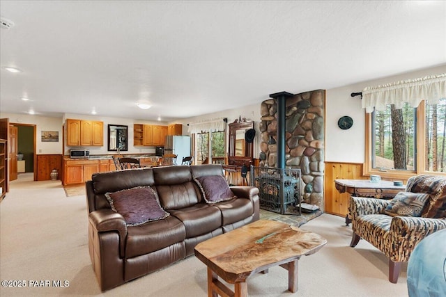 living room with light colored carpet, a wood stove, a healthy amount of sunlight, and a wainscoted wall