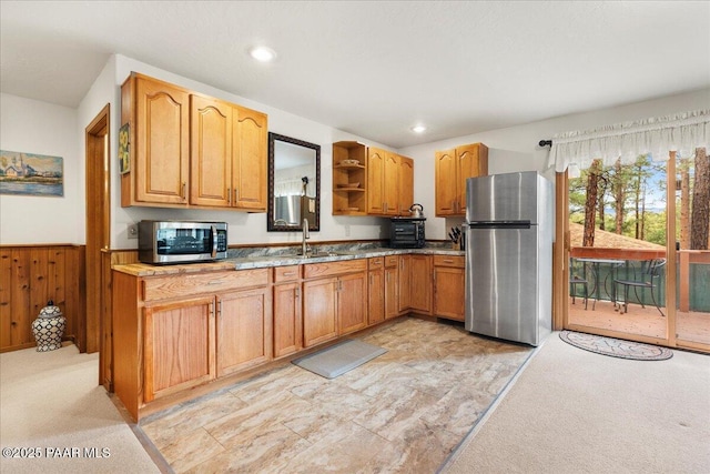 kitchen with a sink, wood walls, light colored carpet, stainless steel appliances, and open shelves