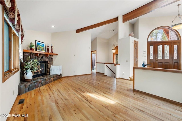 unfurnished living room with a stone fireplace, lofted ceiling with beams, wood finished floors, and visible vents