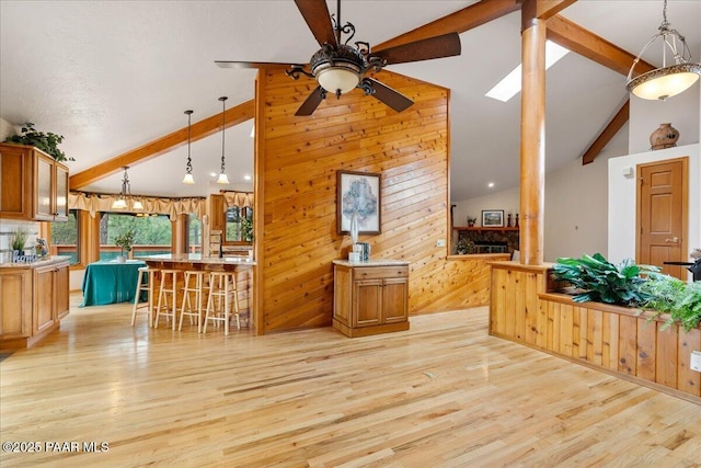 kitchen featuring beam ceiling, light wood-type flooring, wood walls, and ceiling fan