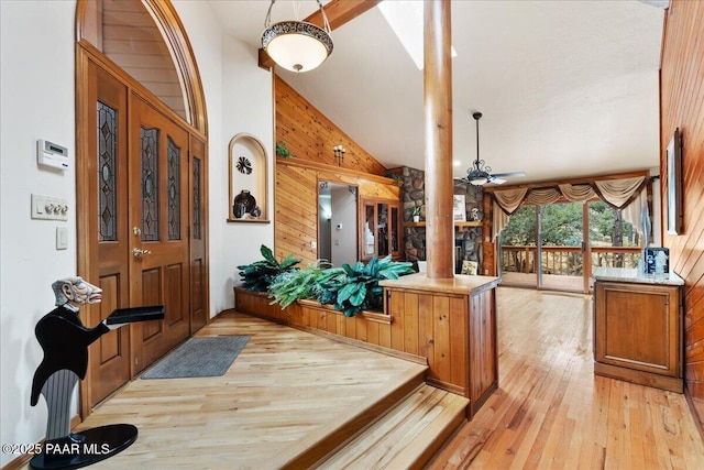 foyer featuring light wood-style flooring, wood walls, ceiling fan, and decorative columns