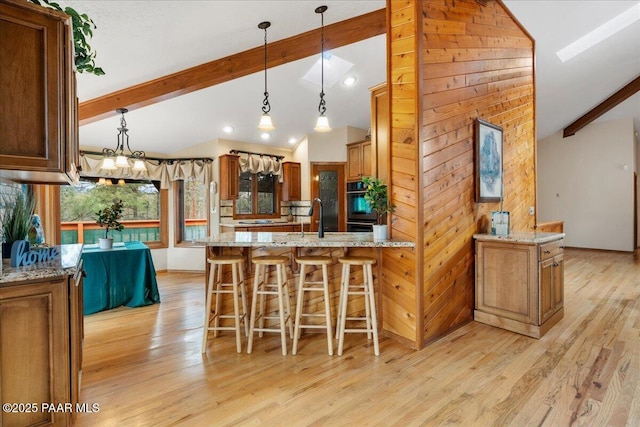 kitchen with beam ceiling, a peninsula, light wood-style flooring, and light stone countertops