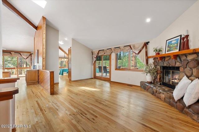 living area with a healthy amount of sunlight, light wood-style flooring, a fireplace, and vaulted ceiling